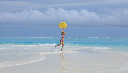 Canvas Print - girl in a bikini with a yellow umbrella on the sea sand