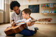 © Drazen - Little boy learns to play acoustic guitar with help of his preschool teacher.