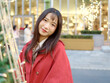 Portrait of beautiful Chinese girl with black long hair in red Christmas clothes smiling at you with city street background, Outdoor fashion portrait of glamour young Chinese cheerful stylish woman.