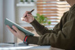 © wattana - Cropped view of young man sitting at home office desk and making notes on notebook.