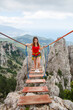 A young girl walks across a suspension bridge on an abyss in the mountains against the backdrop of the sea on a sunny summer day.Safe adventures while traveling, healthy image zhini concept