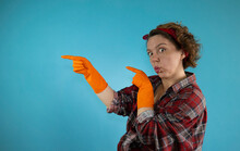 An Adult Pin-up Woman In A Plaid Shirt Shows Her Hands On A Blue Background In A Plaid Shirt. Portrait Of Woman Cleaning Pin-up. Woman In Orange Cleaning Gloves