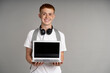 Ginger male student showing screen of laptop at grey background