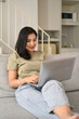 © Prathankarnpap - Happy young woman in casual clothes surfing internet on laptop, enjoying leisure weekend time at home