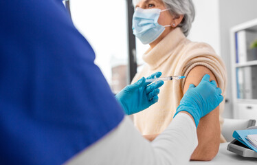 Canvas Print - medicine, health and vaccination concept - close up of doctor or nurse with syringe making vaccine or drug injection to senior woman in mask at hospital