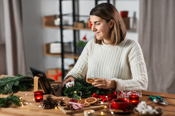 Poster - winter holidays, diy and hobby concept - happy smiling woman with tablet pc computer making christmas fir wreath at home