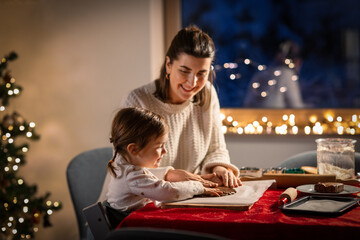 Poster - family, cooking and winter holidays concept - happy mother and baby daughter having fun with dough for gingerbread cookies at home on christmas