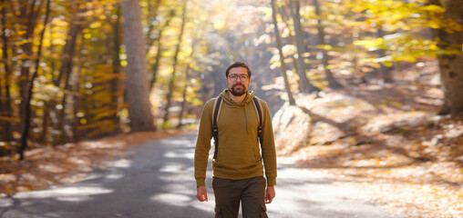 Young handsome man posing in autumn forest. young hipster guy with backpack , traveller standing in woods, Hiking, Forest, Journey, active healthy lifestyle, adventure, vacation concept.