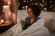 © Syda Productions - people, bedtime and rest concept - happy smiling woman in pajamas with coffee sitting in bed at night