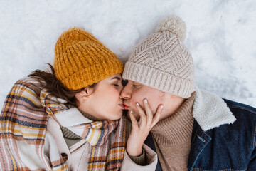 Poster - people, love and leisure concept - happy couple kissing lying on snow in winter