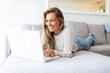 © Dragana Gordic - Communication is very important. Top view portrait of young smiling woman sitting on sofa at home with laptop laying on back-rest. Business woman working from home