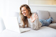 © Dragana Gordic - Smiling young woman in knitted sweater freelancer working from home, sitting on couch, using laptop, copy space. Relaxed lady enjoying her weekend, surfing on internet on laptop