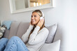 © Dragana Gordic - Shot of a young woman using headphones while relaxing on the sofa at home. Nothing evokes memory like music. Side view of young woman listening to music online