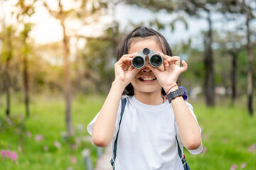 Wall Mural - Children travel in flower field and holding binoculars on green nature background