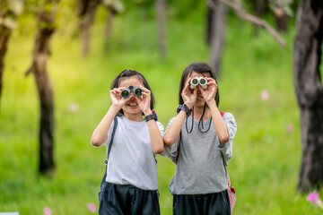 Wall Mural - Children travel in flower field and holding binoculars on green nature background