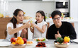 © atitaph - A happy Asian family spends lunch, vegetables, fruit, and dates at the table in their home. Cute little daughter having fun talking. Father, mother