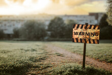 A Yellow Sign With The Word "warning" Stuck Into The Ground In Front Of An Old Abandoned Building At Sunset On A Cloudy Day
