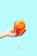 Aperol Spritz cocktail on a girls hand on blue background