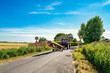 © Nick Beer - Distant farm tractor and trailer seen entering a rural village with a 30Mph zone. The uneven asphalt road is clearly evident due to heavy farm vehicles.