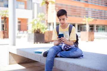 Caucasian teenage student boy using a smart phone outdoors. Space for text.