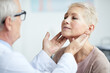 © Mediaphotos - Over shoulder view of senior endocrinologist touching neck of mature female patient while examining her thyroid