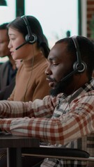 Wall Mural - Vertical video: African american employee using headphones to talk to clients, helping with sales and giving telemarketing assistance at call center. Male operatortalking to people in disability