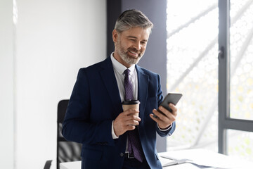 Portrait Of Smiling Mature Businessman Resting In Office With Smartphone And Coffee