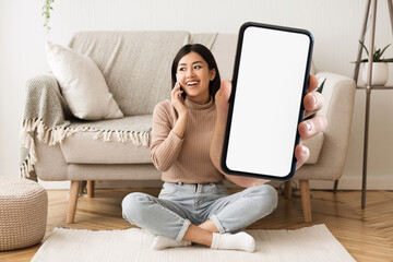 Wall Mural - Happy Asian Woman Talking On Phone And Showing Blank Smartphone At Camera