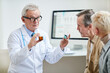 © Mediaphotos - Confident handsome aged physician in lab coat and glasses holding two pill bottles and explaining difference between drugs to patients