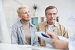 © Mediaphotos - Content senior couple in casual outfits sitting in doctors office and listening to attending physician at consultation