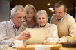 © Mediaphotos - Group of curious elderly former classmates in casual clothing sitting at table and watching old photos on tablet