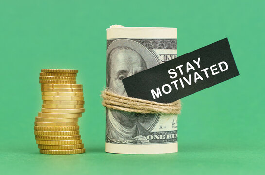 On a green surface are coins and dollars in a bundle. On the dollar sign with the inscription - Stay Motivated