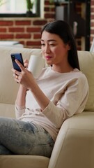 Wall Mural - Vertical video: Happy woman sending messages on mobile phone while doing work from home and listening to music. Joyful person texting coworker on touchscreen phone while working remotely. Handheld