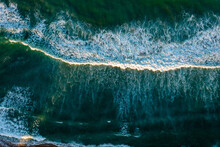 
Aerial View Of A Wave Breaking In The Outer Banks As A Strand Of Golden Sunshine Breaks Through The Clouds On The Ocean