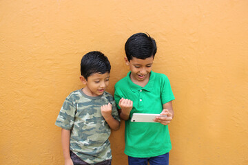 two dark-haired latino male children living in poverty use their cell phones to play games and are e