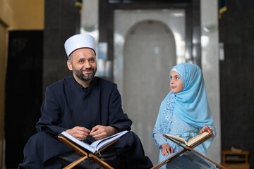 Wall Mural - A Muslim teacher teaching a child girl to read a holy book Quran inside the Mosque. Happy Islamic family.