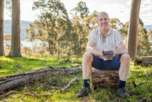 Smiling Man Sitting On A Log In The Bush