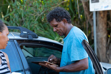 Man And Woman Next To Car With Man Looking At Digital Tablet