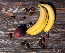 Composition Of Ripe Bananas, Appetizing Peach And Dried Dates, On A Dark Brown Wooden Textured Table, For Your Design Or Illustrations.