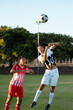 Full length of multiracial male players chasing soccer ball in mid-air against clear sky in match