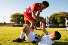 Multiracial Player Giving Hand To Injured Opponent Lying On Field In Getting Up Against Clear Sky
