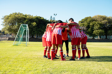 Male multiracial players in red uniform with arms around discussing and huddling at playground