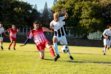 Poster - Male multiracial players running and kicking the soccer ball during match at playground in summer