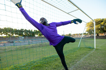 Wall Mural - African american male goalkeeper with arms raised jumping and catching soccer ball during match