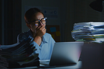 Overworked young Asian office employee yawn during working on laptop computer overtime at night in office