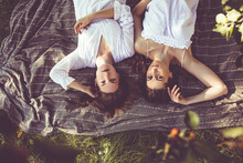 Couple Of Young Beautiful Girls Resting On A Blanket In A Park In Nature In Summer, Top View