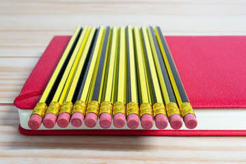 Wooden 2b pencils lying on red note book on wooden table. Copy space.