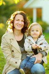 Sticker - Cute funny toddler boy in his mothers arms. Mom and son having fun on sunny autumn day in a park.