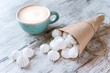 Small white meringue in the paper bag, cup of coffee with cream on the rustic background