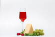 a glass of red wine on a white background with raspberry cheese and grapes